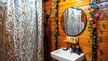 A bathroom with a wooden wall, a shower curtain, a sink, a mirror, and decorative foliage.