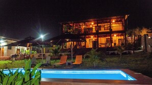A two-story building with a swimming pool, outdoor seating, and a well-lit patio area. - Seaview Cabana (Winneba)