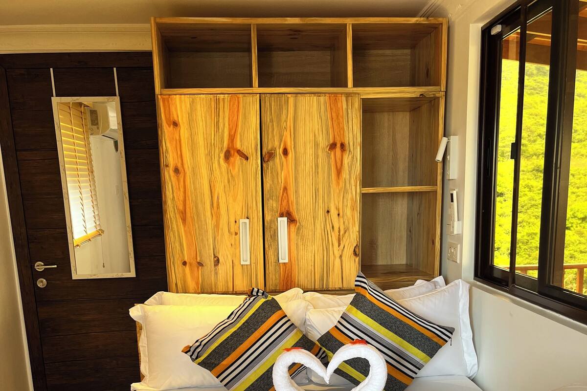 Quarto de hotel com uma cama grande, guarda-roupa de madeira, um espelho e uma janela com vista para áreas verdes.