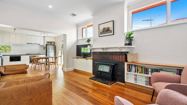 A modern living room with a fireplace, a dining area, and a kitchen with white cabinets. - New Town Bungalow A Leafy Family Haven (New Town)