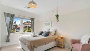 A bedroom with a bed, bedside table, chair, and a hanging plant. - New Town Bungalow A Leafy Family Haven (New Town)