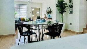 A dining area with a round glass table and black chairs, a potted plant, and a staircase leading to another room. - Azores Luxury Residence

 (Borinquen)