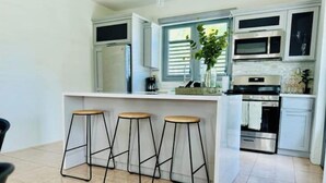 A modern kitchen with white cabinets, a central island with stools, a stainless steel refrigerator, and a built-in oven. - Azores Luxury Residence

 (Borinquen)