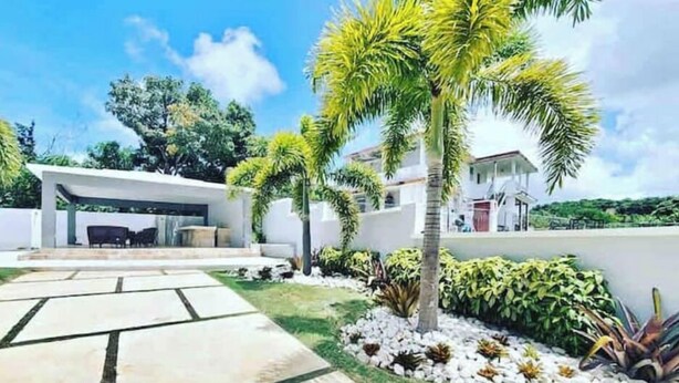 A modern house with a covered patio, a stone pathway, and tropical plants. - Azores Luxury Residence

 (Borinquen)