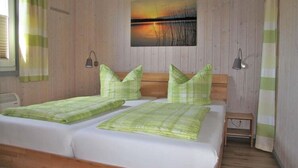 A double bed with green bedding, a wooden headboard, and a painting of a sunset on the wall.