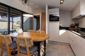 A modern kitchen with a dining area, including a round wooden table, wicker chairs, and built-in appliances. - Docklodge in Friesland With Private Mooring (Delfstrahuizen)