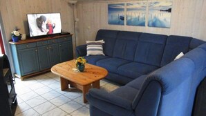 A living room with a blue sofa, a wooden coffee table with a vase, a television on a cabinet, and a painting on the wall. - Exklusives Skandinavisches Ferienhaus (Mirow)