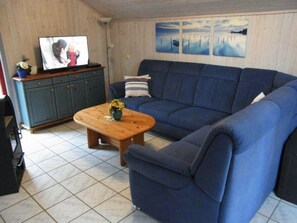 A living room with a blue sofa, a wooden coffee table with flowers, a television on a stand, and a cabinet with a vase.