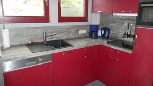 A kitchen with red cabinets, a stainless steel sink, a coffee maker, and a window with a view of greenery. - Exklusives Skandinavisches Ferienhaus (Mirow)