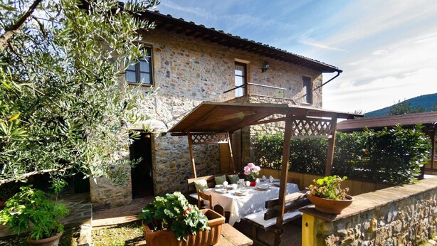 A stone building with a covered patio area, potted plants, and a table set for dining. - Spacious Cottage in Buti (Buti)
