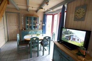 A dining area with a wooden table and chairs, a television displaying a house, and a blue cabinet with glass doors.