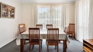 A dining area with a table set for six, wooden chairs, a painting on the wall, and large windows with sheer curtains. - Classic Retro Home Steps from Sandy Bays Best (Sandy Bay)