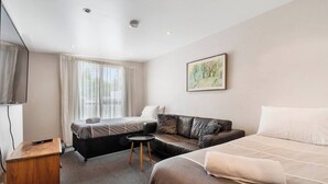 A hotel room with a bed, a sofa, a small table, a TV, and a window with curtains. - Classic Retro Home Steps from Sandy Bays Best (Sandy Bay)