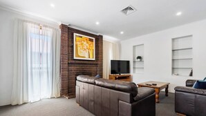 A modern living room with a sectional sofa, a flat-screen TV, and a fireplace. - Classic Retro Home Steps from Sandy Bays Best (Sandy Bay)