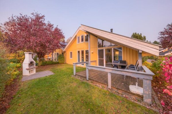 A yellow house with a deck, a barbecue, and a garden. - Exklusives Skandinavisches Ferienhaus (Mirow)
