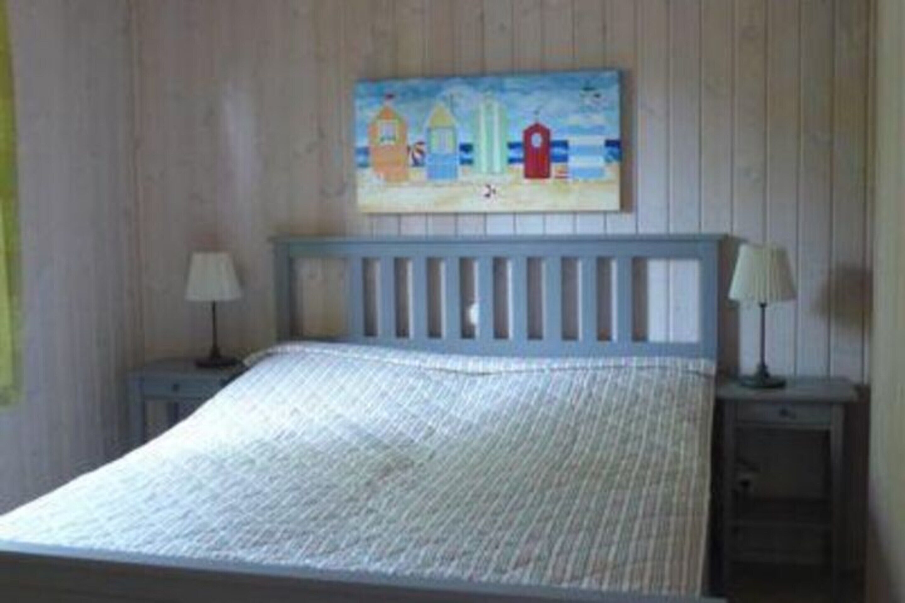 Une chambre à coucher avec un lit, deux tables de chevet et un tableau représentant une scène de plage accroché au mur.