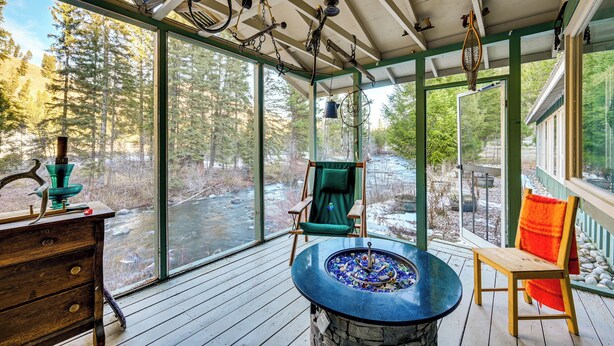 A wooden deck with a stone fireplace, a green chair, and a wooden table. - 22 Mi to Lost Trail Skiing: Serene Winter Retreat (Sula)