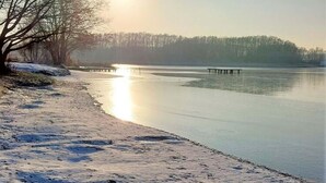 Un lac gelé avec une jetée en bois qui s’avance sur l’eau, entouré d’arbres sans feuilles et sous un ciel dégagé.