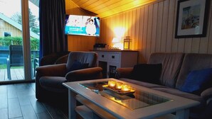Un salon confortable avec un téléviseur à écran plat, une table basse en verre ornée de bougies et un canapé.