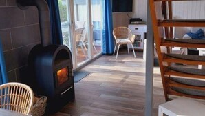 Une pièce chaleureuse avec un poêle à bois, des fauteuils en osier et une vue sur l’extérieur.