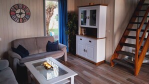 Un salon avec un canapé beige, une table basse en verre ornée de bougies, un meuble blanc et un escalier en bois.