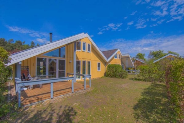 A yellow house with a large deck, a chimney, and a clear blue sky.