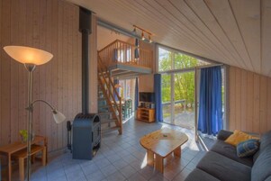 Ein großzügiger Wohnbereich mit hoher Decke, einer Holztreppe, einem Kamin, einer Couch und einem großen Fenster mit Vorhängen.