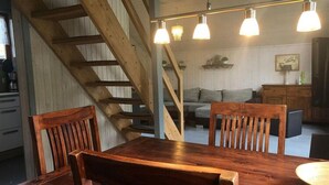 A wooden dining table with chairs, a staircase, and pendant lights in a room with a sofa and cabinets. - Ferienhaus im Skandinavischen Stil (Mirow)