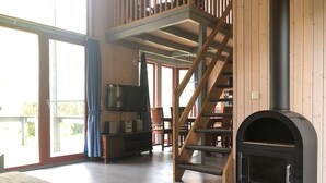 A spacious living area with a wooden staircase, a fireplace, a television, and a large window. - Ferienhaus im Skandinavischen Stil (Mirow)