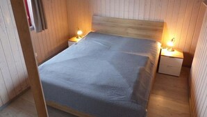 Une petite chambre accueillante, avec un lit simple, deux tables de chevet avec des lampes, des murs en bois et un tableau accroché au mur.