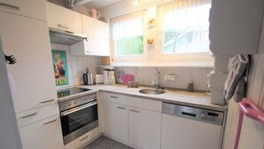A compact kitchen with white cabinets, a stainless steel oven, a dishwasher, and a window with curtains. - Exklusives Skandinavisches Ferienhaus (Mirow)