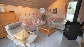 A cozy living room with a sofa, armchair, and coffee table, a fireplace, and wooden walls. - Exklusives Skandinavisches Ferienhaus (Mirow)