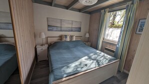 A bedroom with a large bed, a nightstand, a wall-mounted lamp, and a window with curtains. - Exklusives Skandinavisches Ferienhaus (Mirow)