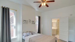 Ein Schlafzimmer mit Bett, Deckenventilator und einem durchgehenden Türspalt sichtbarem Badezimmer.