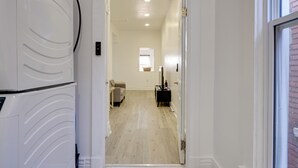 Ein Flur mit einer weißen Tür, die zu einem Raum mit Holzboden, einem kleinen Tisch und einem Stuhl führt.