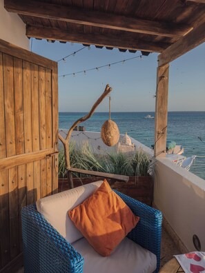A wooden deck with a wicker chair and cushions, overlooking a calm sea with a boat in the distance. - La Gotera (Los Roques)