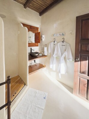 A bathroom with a wooden vanity, a sink, a mirror, and two white robes hanging on hooks. - La Gotera (Los Roques)