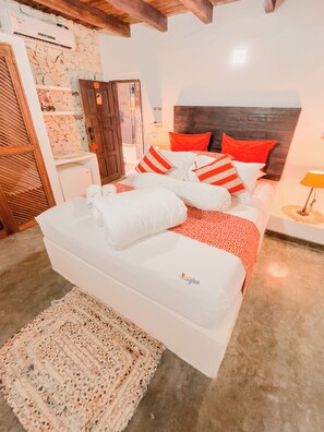 A bed with white and red bedding, a wooden headboard, and a small bedside table with a lamp. - La Gotera (Los Roques)