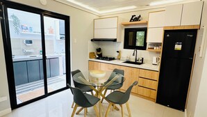 Een moderne keuken met een eethoek, met een glazen tafel en stoelen, een zwarte koelkast en een bordje met de tekst 'Eat'.