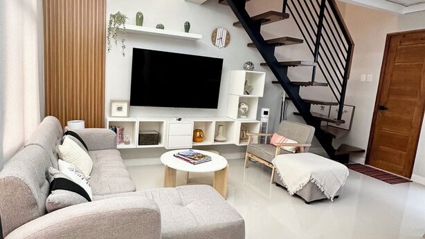 Een moderne woonkamer met een hoekbank, een flatscreen televisie, een trap en een minimalistisch design.