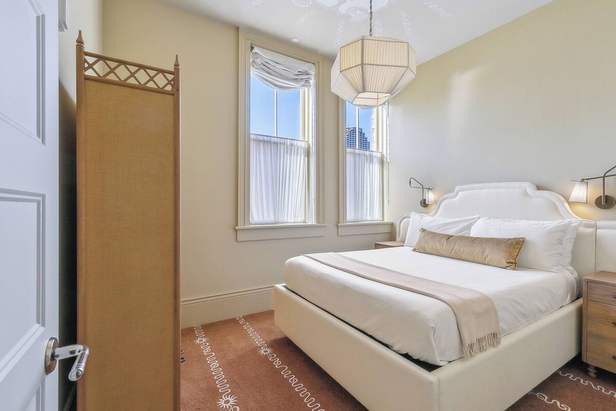 A bedroom with a bed, bedside lamps, a window with curtains, and a hanging light fixture.