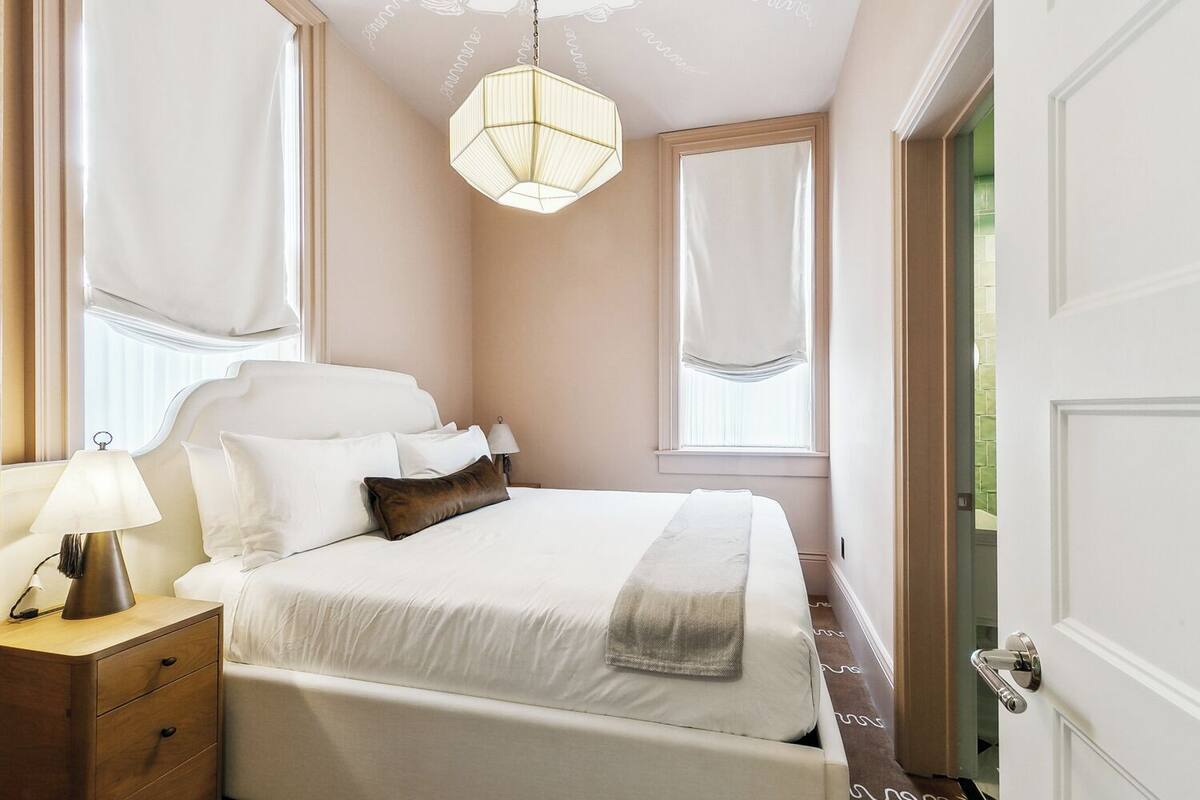 A neatly arranged bedroom with a large bed, bedside tables, a hanging light fixture, and a window with curtains.