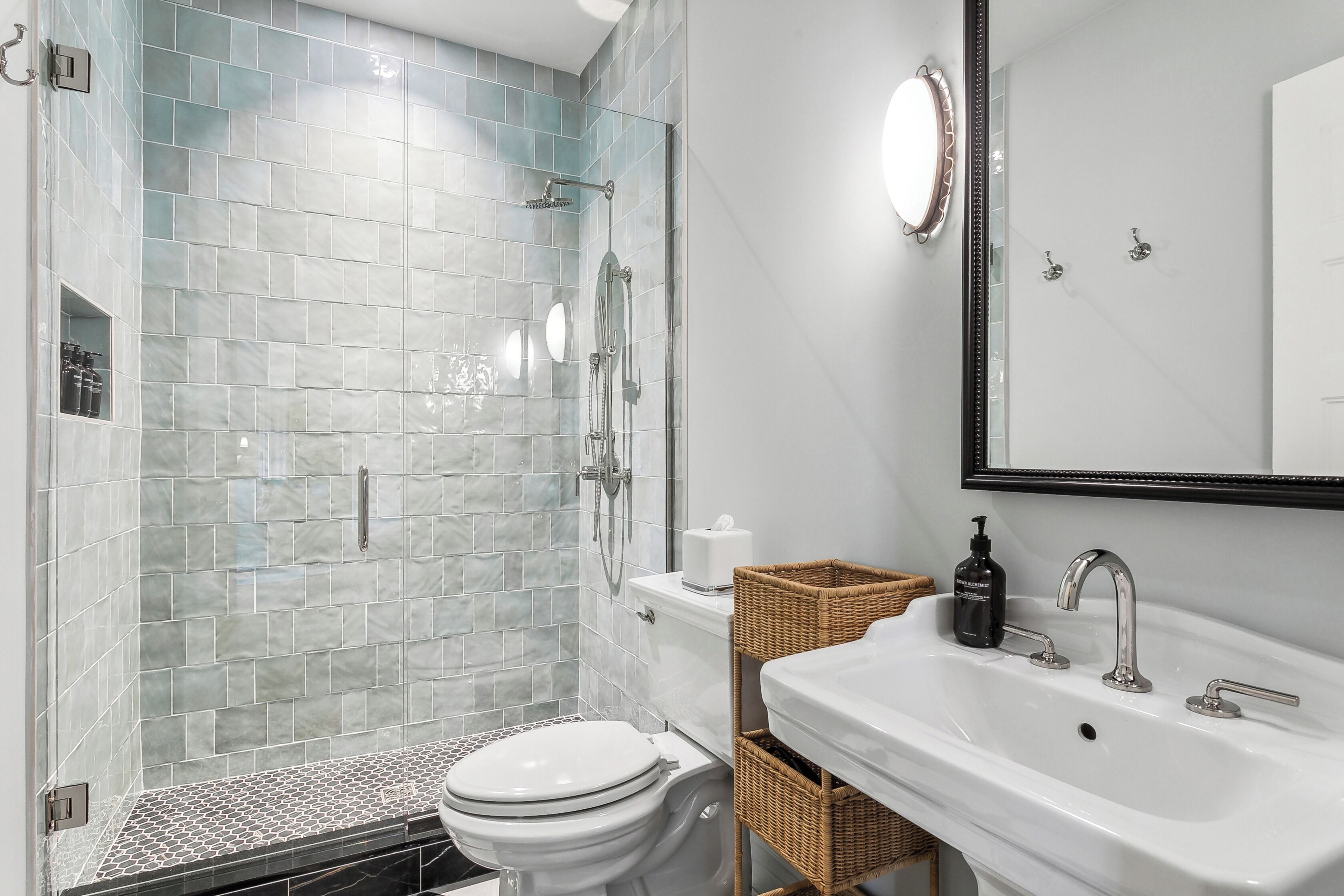 Een badkamer met een glazen douchecabine, een wit toilet, een wastafel met spiegel en rieten manden.