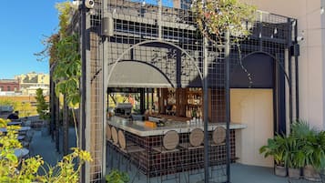 A rooftop bar with outdoor seating, a bar counter, and a view of the cityscape.