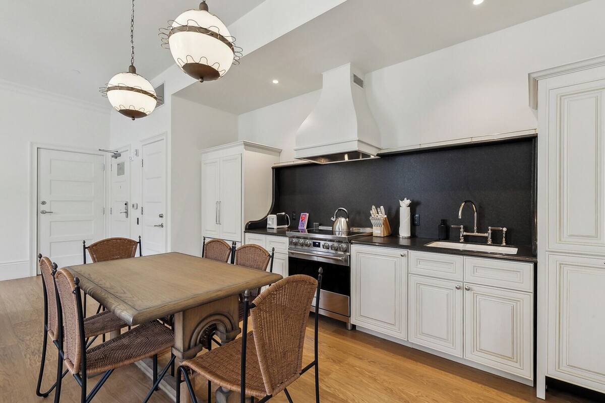 A modern kitchen with white cabinetry, a black backsplash, stainless steel appliances, and a dining area with wicker chairs and a wooden table.