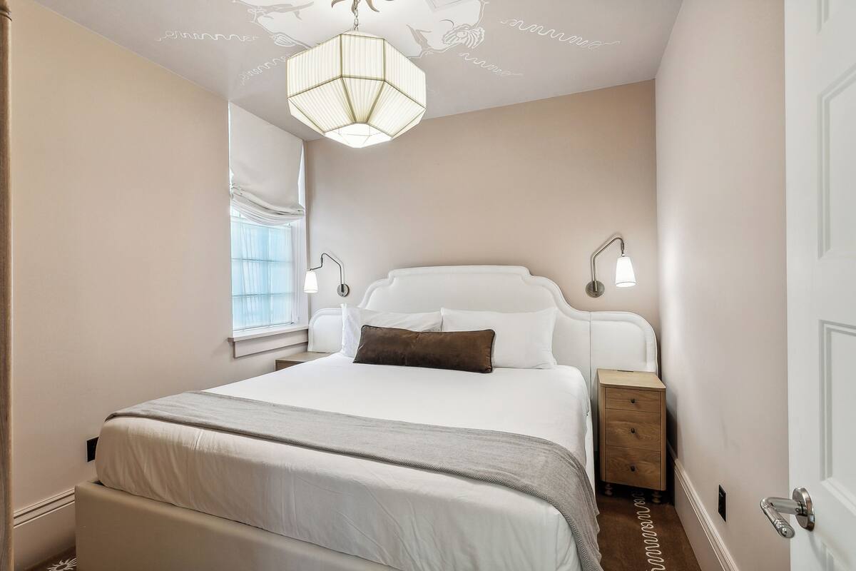 A neatly arranged bedroom with a large bed, bedside lamps, and a hanging light fixture.
