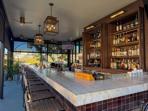Een bar met een marmeren aanrecht, rieten stoelen en verschillende flesjes drank.