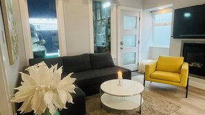 Una sala de estar con un sofá, un sillón amarillo, una mesa de centro blanca y un jarrón verde con flores blancas.