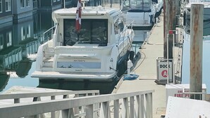 Un puerto deportivo con barcos amarrados, un horizonte urbano al fondo y un puente con barandilla en primer plano.