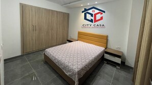 A bedroom with a bed, a wardrobe, a nightstand, and a logo on the wall. - S+2 apartment for rent 15 minutes from the beach on foot  (Mrezga)
